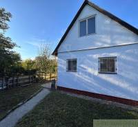 A white cottage with shutters in a yard surrounded by greenery, a typical Slovak scenery.