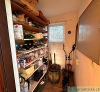A small cellar with shelves filled with supplies, drinks, and tools near the cottage.