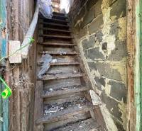 Old wooden stairs lead to the attic, surrounded by the shabby walls of the old house and cottage.