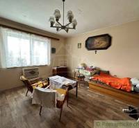 A room in a family house with armchairs, a bed, wooden flooring, and wall decorations.