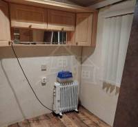 A room in a family house with a radiator, shelves, light-colored cabinets, wooden floor, and curtains.