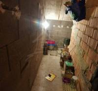 A narrow basement of a family house with cardboard boxes and bottles, concrete and brick walls.
