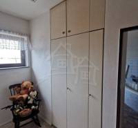 A room in a family house with a white wardrobe, toys on a chair, and a window with a curtain.