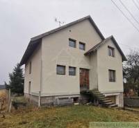 A family house with a concrete foundation, surrounded by a grassy plot, stairs leading to wooden doors.