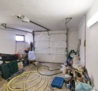 A garage with stored items, a hose, and a family house in the background.