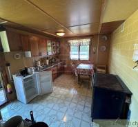 A kitchen with a wooden cabinet, an old stove, and an open refrigerator in a family house.