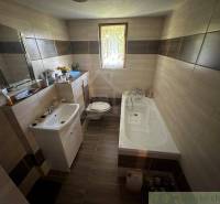 A bathroom with a bathtub and a sink in a family house, surrounded by tiles.