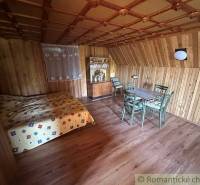 Wooden interior in a family house with a bed, table, and chairs, cozy environment.