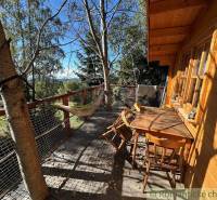 Wooden terrace with a swing and a table, surrounded by nature near a family house.