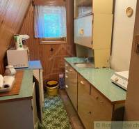 A country kitchen in the attic with wooden paneling, a window, kitchen cabinets, and appliances.