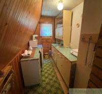 Narrow wooden kitchen with a refrigerator, cabinets, and a window in a family house.