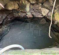 A stone well with water surrounded by stones, a natural feature near a family house.