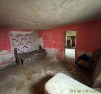 A room in a family house with a bed, damaged plaster, and a colorful wall.