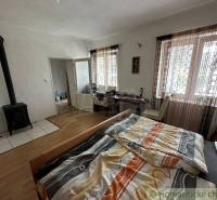 A room in a family house with a tiled stove, a bed, curtains, and large windows.