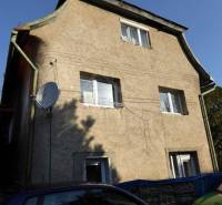 Stone family house with three floors, windows, and a satellite dish, surrounded by cars.