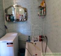 A bathroom with green tiles, a washing machine, a mirror, and a lot of cosmetics. Family house.