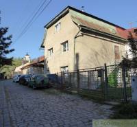 A family house with a metal roof by the road, surrounded by cars and a fence.