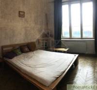 Bedroom in a two-room apartment, bed, window, curtains, minimalist wooden furniture.