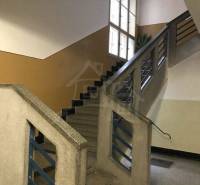 A staircase in an apartment building with windows and a railing, leading to apartment doors.