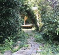 A romantic garden with unique properties, a stone path leads to a wooden gazebo surrounded by greenery.