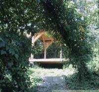 A comfortable wooden gazebo in nature, surrounded by lush greenery and peculiar properties.