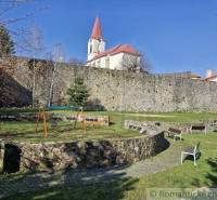 A children's playground with swings near a historic church and a stone wall in the park.