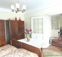 A room with a wooden wardrobe, a bed, a table decorated with flowers; a typical cottage.