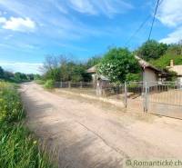 The path leads past a romantic cottage surrounded by nature and shrubs, under a blue sky.