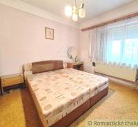 A bedroom with a double bed in a family house, decorated with simple furniture and curtains.