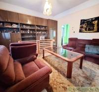 A living room in a family house with rustic furniture, red armchairs, and a wooden bookshelf.