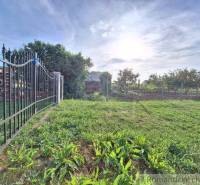 The gate leads to a vast, sunny garden with a lawn and trees.