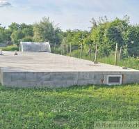 A concrete foundation slab in a garden environment, surrounded by grass and trees.