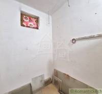 A small room in a cottage with white walls, a window with a patterned curtain.