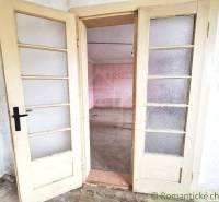 Worn double doors leading to a room with pink walls in a cottage.