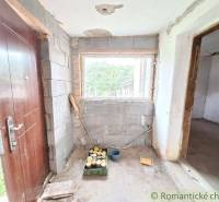 A cottage under reconstruction with wooden doors, a window without glazing, and an entrance to the room.