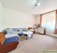Living room in a family house with an upholstered sofa, a table, and windows with curtains.
