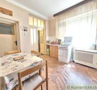 Dining room and kitchen in a family house with a table, chairs, a gas stove, and large windows.