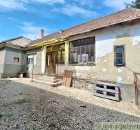 A family house with plaster needs renovation, a stone-covered yard, and stairs.
