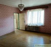 A room with older patterned wallpaper, wooden flooring, and a chandelier.