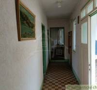 A hallway in a family house with a tiled floor, a painting, and a window for natural light.