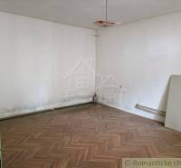 A room with a damaged floor, white walls, and an old light fixture, family house.