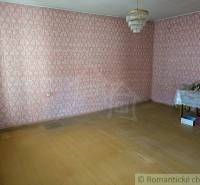 A room with patterned wallpaper, a simple light fixture, wooden flooring, and a table in a family house.
