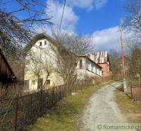 I see an older family house surrounded by nature, a driveway, and a blue sky.