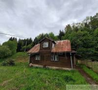 A cottage in Veľké Rovné surrounded by greenery, bordered by an old fence and trees.