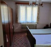 A bedroom in a cottage with a wooden wardrobe, carpet, and two beds under the window.
