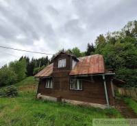 A wooden cottage in Veľké Rovné surrounded by greenery and a slightly cloudy sky.