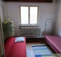 A room with two beds and a small carpet. Through the window, there is a view of nature.
