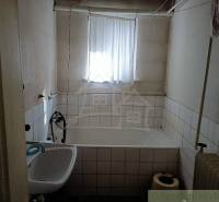 An older bathroom with a bathtub and a sink in a cabin, light through a small window.