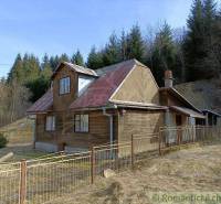 A cottage in Veľké Rovné with a wooden exterior and a metal fence in a forest environment.