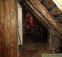 A dark attic hallway in a cabin with slanted wooden walls and electrical wires.